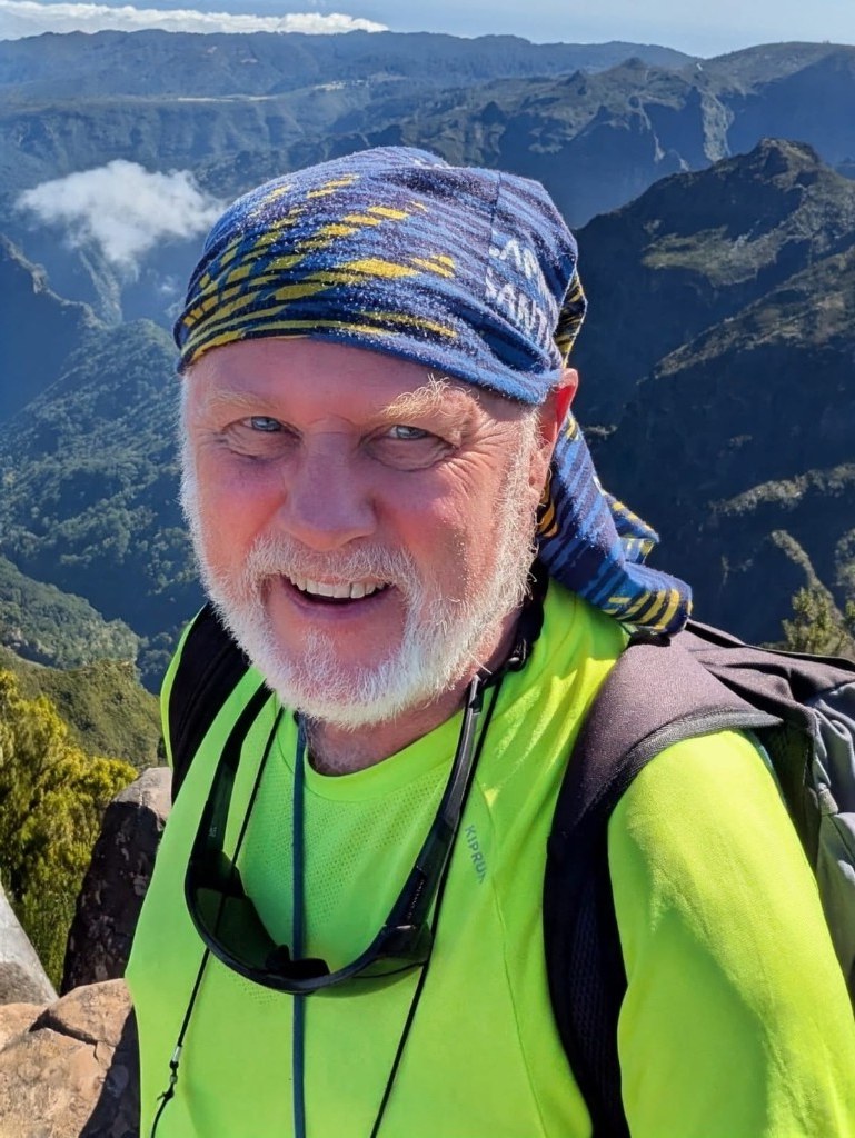 Andrew Considine on the Camino — yellow shell bandana, trekking gear and hills behind him